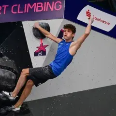 Mejdi Schalck, jeune grimpeur en action sur un mur de bloc, saisit une prise avec détermination.
