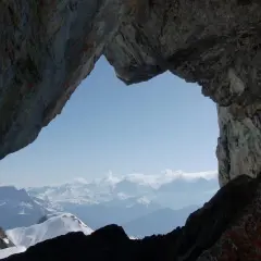 Vue spectaculaire sur les montagnes enneigées depuis le "Trou de la Mouche", un passage rocheux offrant une perspective unique lors d'une randonnée.