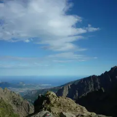 Vue spectaculaire sur la mer depuis les montagnes escarpées du GR20 partie nord. Le ciel bleu est parsemé de nuages blancs.