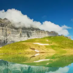 Reflets parfaits d'une montagne imposante et d'une colline verdoyante dans un lac alpin paisible, évoquant la sérénité du tour des Fiz.
