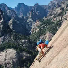 Un grimpeur en plein effort sur un rocher, avec les majestueuses montagnes de Bavella en arrière-plan. L'escalade bavella offre des vues spectaculaires.