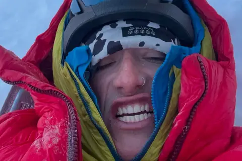 Balin Miller, le visage crispé par le froid, emmitouflé dans sa doudoune rouge et jaune, prêt pour l'aventure.