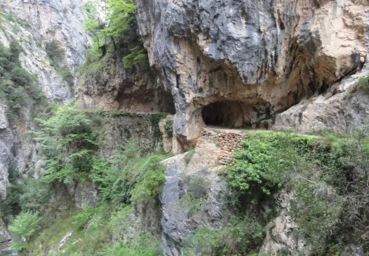 Sentier creusé dans la roche, le long de la ruta del Cares dans les Picos de Europa. Un tunnel naturel s'ouvre sur le chemin.