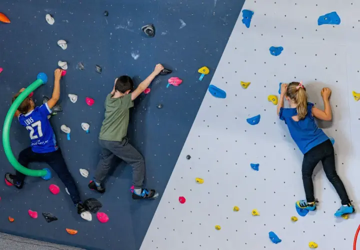 Trois enfants s'amusent lors d'une bloc session à Vienne, grimpant sur un mur coloré avec des prises variées.