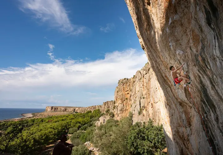 Un grimpeur défie la falaise en Sicile, avec la mer et la végétation en toile de fond. L'escalade sicile offre des vues spectaculaires.