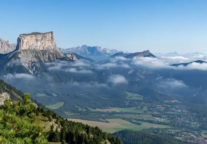 Vue panoramique du Vercors en été. Des montagnes majestueuses, des nuages bas et une forêt verdoyante invitent à explorer ce paysage magnifique.