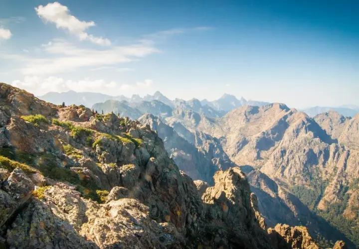 Vue spectaculaire sur la partie sud du GR20, avec des randonneurs sur un sentier rocheux et des montagnes majestueuses à perte de vue.