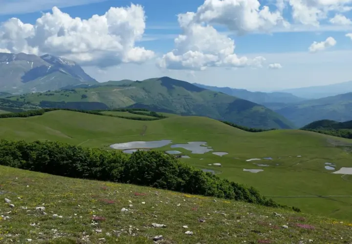 Vastes prairies verdoyantes parsemées de petits étangs dans le parc national des Monts Sibyllins, sous un ciel bleu et nuageux.