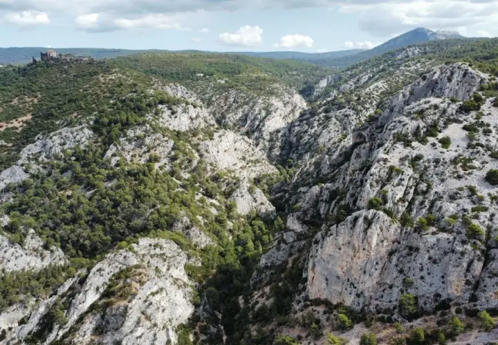 Vue aérienne de la **gorge d'Ollioules**, un canyon rocheux bordé de pins, avec un château en ruines sur une colline au loin.