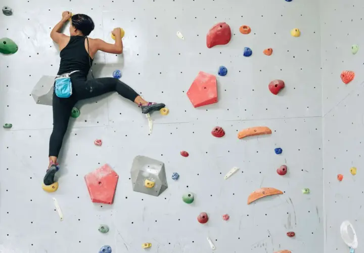 Grimpeuse en action, un pied dans la main, sur un mur d'escalade coloré. Elle progresse avec agilité.