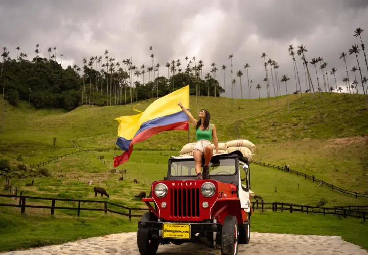 Femme sur une jeep rouge, drapeau colombien flottant, au milieu des palmiers de cire de la Vallée de Cocora, Colombie.