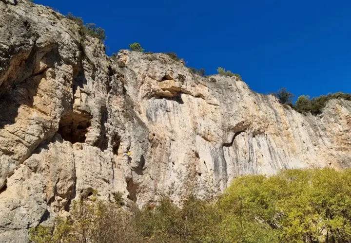 Un grimpeur jaune défie la falaise imposante, un véritable chateauvert pour l'escalade. Le ciel bleu azur surplombe ce paysage rocheux.