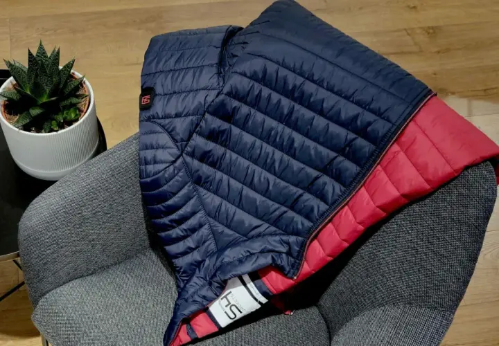 Doudoune bleu marine et rouge pliée sur un fauteuil gris. Une plante verte est posée à côté. Idéal pour redonner du gonflant à une doudoune.