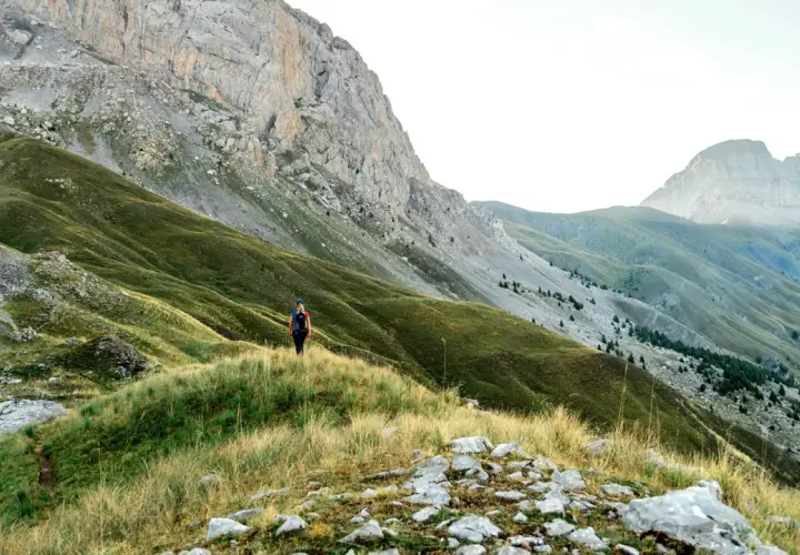 Randonneuse solitaire sur un sentier herbeux, dominant les pentes verdoyantes et les montagnes majestueuses du tour de l'Ubaye.