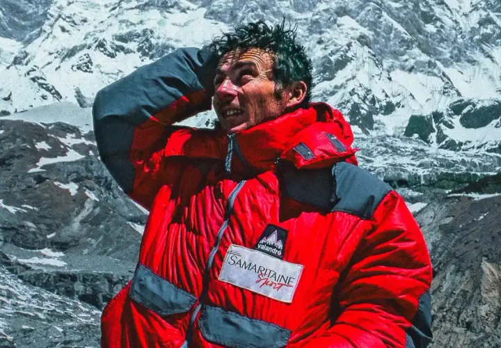 Jean-Christophe Lafaille, le visage marqué par l'effort, se protège du soleil sur fond de montagnes enneigées.
