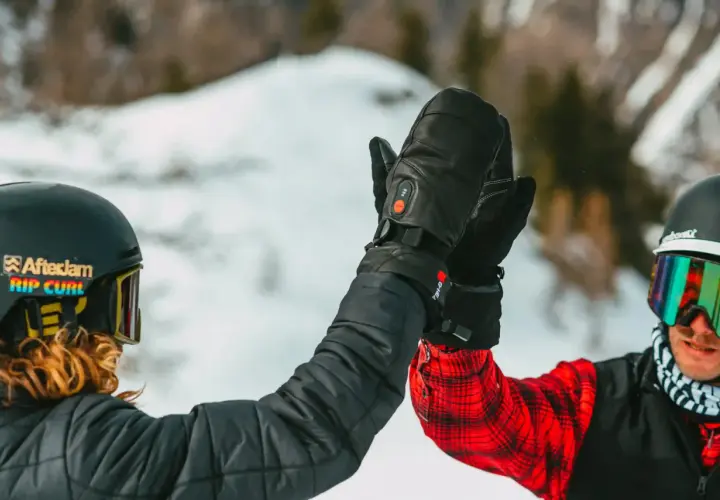 Deux skieurs se donnent une tape dans la main, portant des casques et des lunettes de ski. L'un d'eux a des gants noirs chauffants, une marque de ski de qualité.