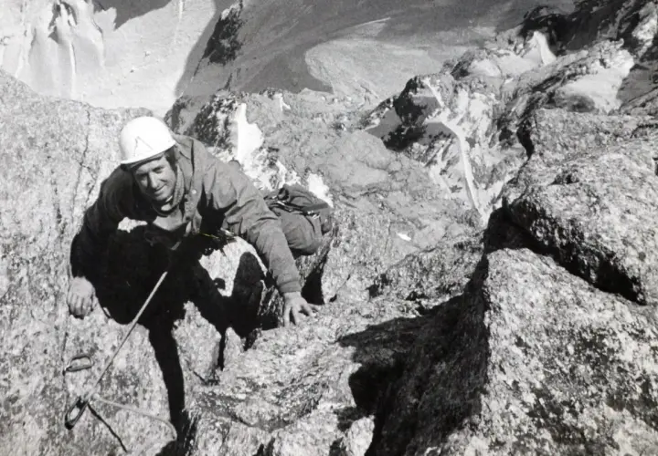 Serge Gousseault, alpiniste chevronné, escalade une paroi rocheuse escarpée, casque blanc sur la tête.