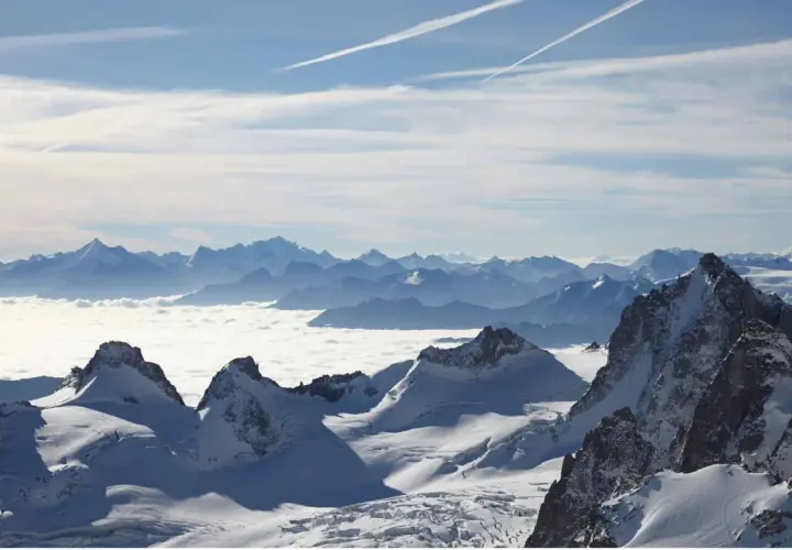 Vue panoramique d'une majestueuse montagne France enneigée, avec des sommets bleutés à l'horizon et une mer de nuages blancs.