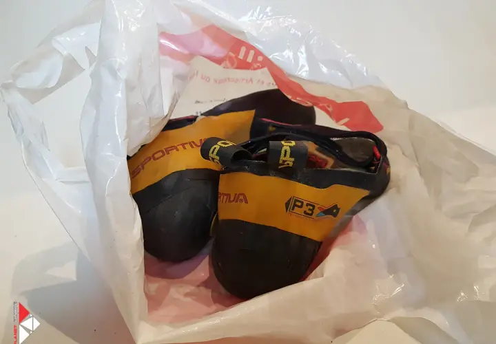 Une paire de chaussons d'escalade Sportiva jaunes et noirs, visiblement un chausson qui pue, dans un sac en plastique blanc.