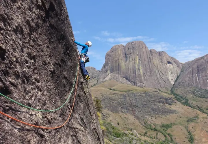 Un grimpeur en pleine ascension sur un rocher impressionnant, avec des montagnes majestueuses en arrière-plan. Une aventure d'escalade à Madagascar.