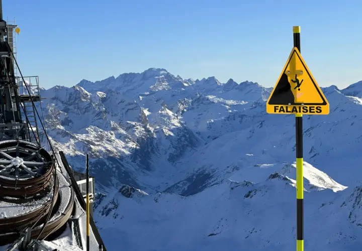 Panneau "Falaises" sur fond de montagnes enneigées, avec une remontée mécanique. Attention aux neiges mouvantes et aux dangers du relief.