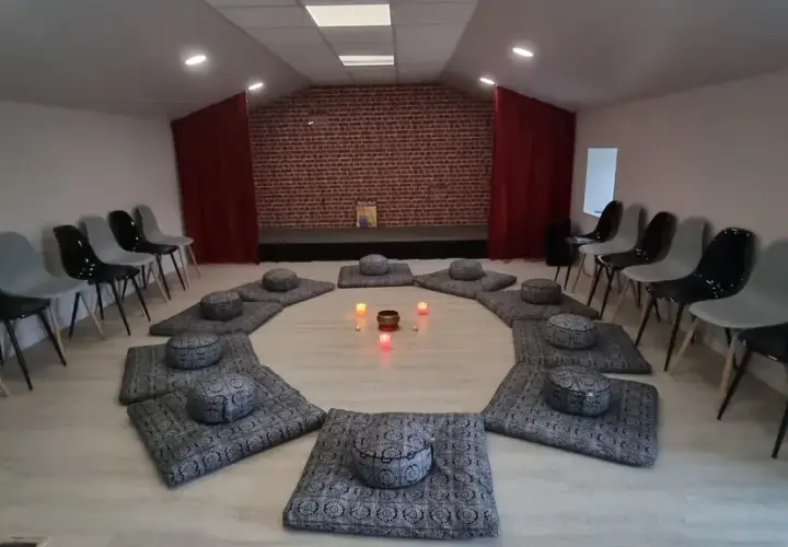 Salle de méditation avec coussins disposés en cercle et bougies allumées. Des chaises attendent autour, créant une atmosphère paisible, comme un refuge au petit goulet.