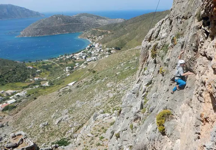 Grimpeur en action sur les falaises de Kalymnos, avec une vue imprenable sur la mer Égée et le village en contrebas.