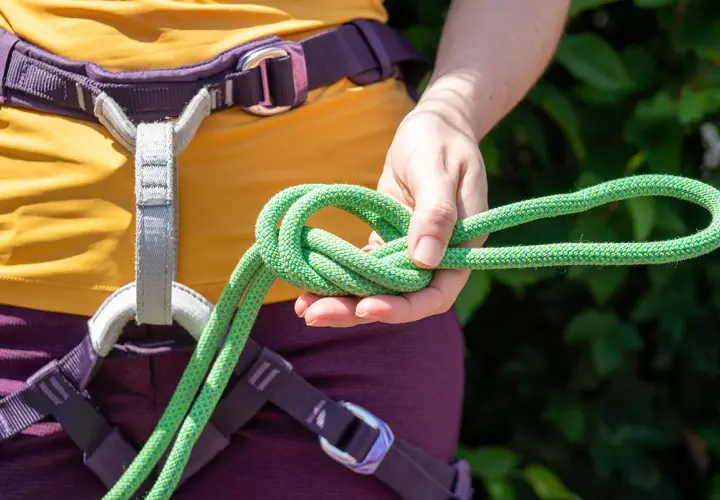 Main d'escaladeuse nouant une cordelette verte, prête pour une longe dynamique.