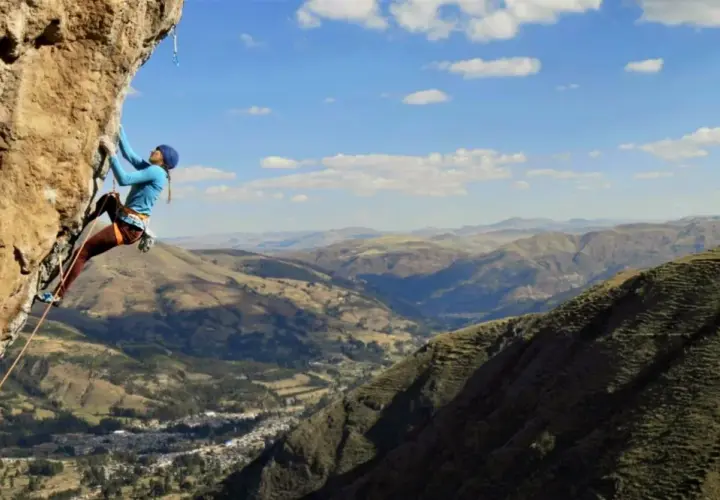 Charlotte Durif, grimpeuse audacieuse, défie la falaise rocheuse sous un ciel bleu. Paysage montagneux spectaculaire en arrière-plan.