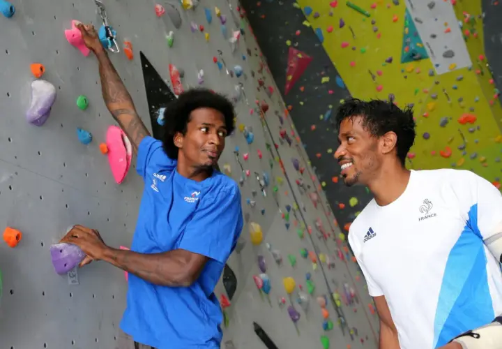 Deux grimpeurs, dont frere mawem, sourient sur un mur d'escalade coloré. L'un est en bleu, l'autre en blanc avec le logo de la France.