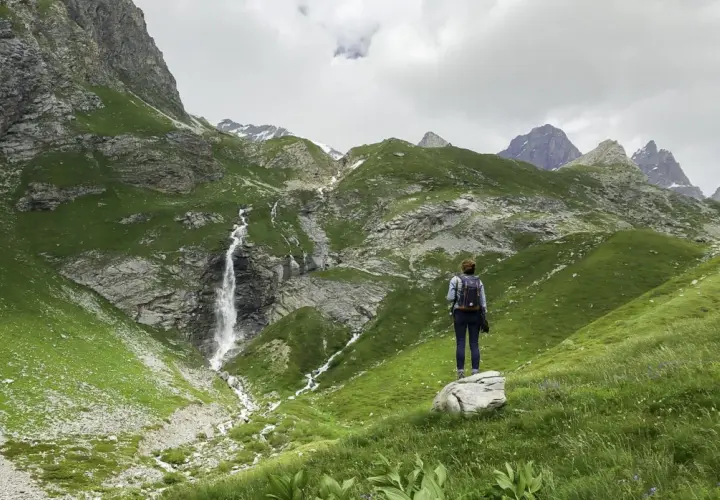 Une randonnée dans les Bauges, avec une cascade impressionnante et des montagnes verdoyantes. Une femme admire le paysage.