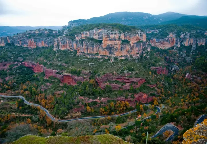 Paysage spectaculaire de falaises rouges et vertes, avec une route sinueuse traversant la vallée. Un paradis pour la siurana escalade.