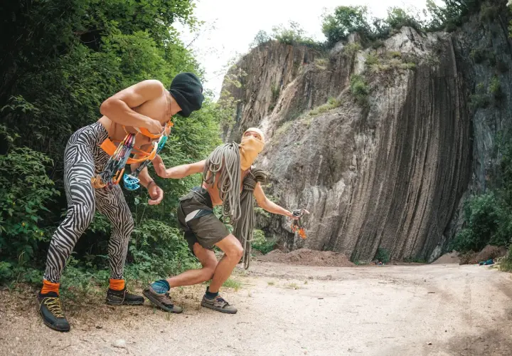 Deux grimpeurs se préparent pour l'escalade dans le Lot, équipés de cordes et de matériel, face à une falaise imposante.