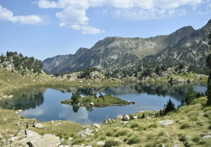 Vue paisible du cirque de Colomers, avec un lac miroir reflétant les montagnes et une petite île verdoyante.