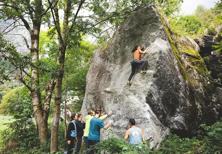 Escalade à Val di Mello : une femme grimpe un rocher pendant que des amis l'encouragent.