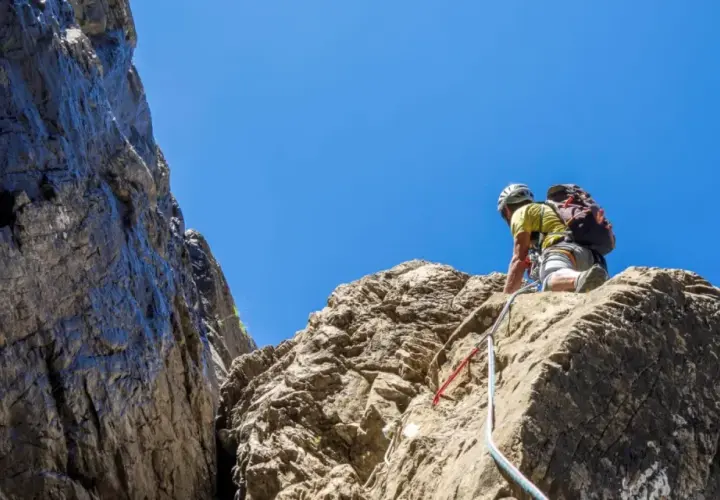 Un grimpeur en plein effort, casque et sac à dos, s'engage sur une paroi rocheuse. L'escalade dans les Pyrénées offre des vues spectaculaires.