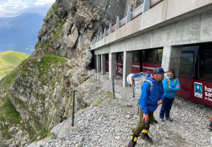 Des randonneurs se tiennent près d'un train rouge, prêts à découvrir comment se rendre au nid d'aigle par ce chemin escarpé.