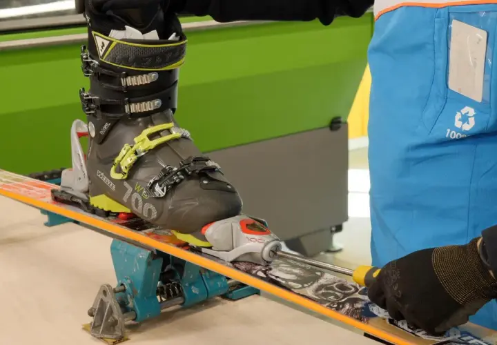 Réglage d'une fixation de ski sur un tableau de fixation. Un skieur ajuste la fixation avec un tournevis.