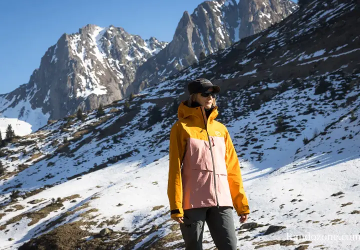 Une femme porte une veste shell colorée, idéale pour affronter les montagnes enneigées.