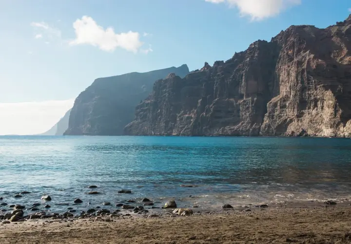 Les falaises de Los Gigantes se dressent majestueusement au-dessus de l'océan bleu. Le rivage est couvert de sable et de galets.