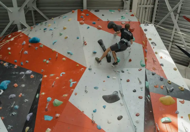 Un grimpeur s'entraîne pour **climb up** sur un mur d'escalade intérieur aux couleurs vives, utilisant des prises variées.