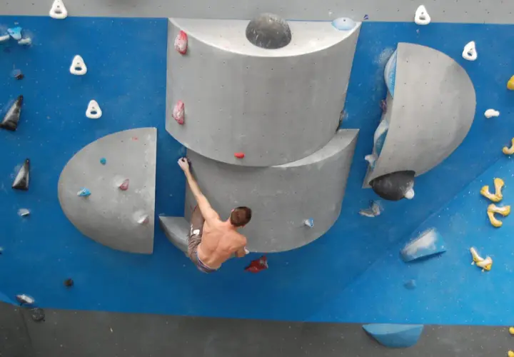 Un grimpeur s'accroche à un bloc escalade, défiant la gravité sur un mur bleu.
