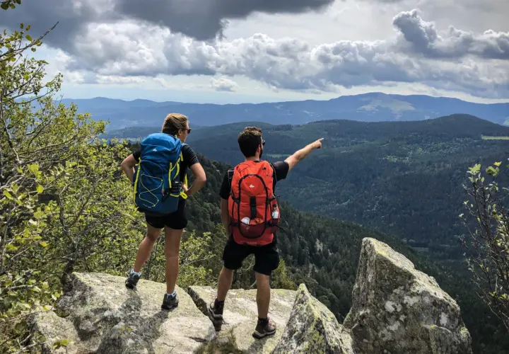 Deux randonneurs contemplent un paysage de montagnes et de forêts. Une balade Vosges facile pour admirer la vue.