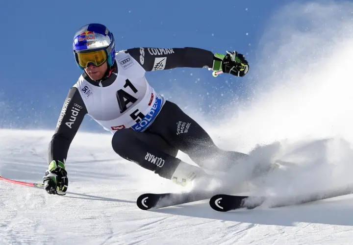 Un skieur acrobatique en plein virage, projetant de la neige avec ses skis rocker. Casque Red Bull, combinaison Colmar.