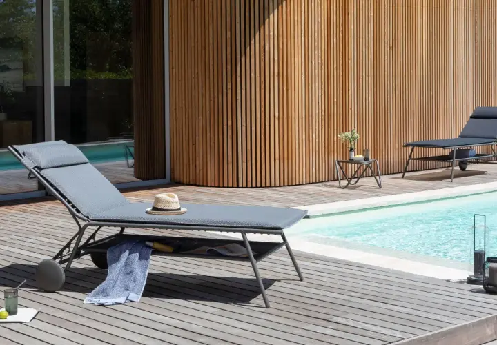 Chaises longues Lafuma près d'une piscine, avec une serviette bleue et un chapeau de paille. Ambiance détente estivale.