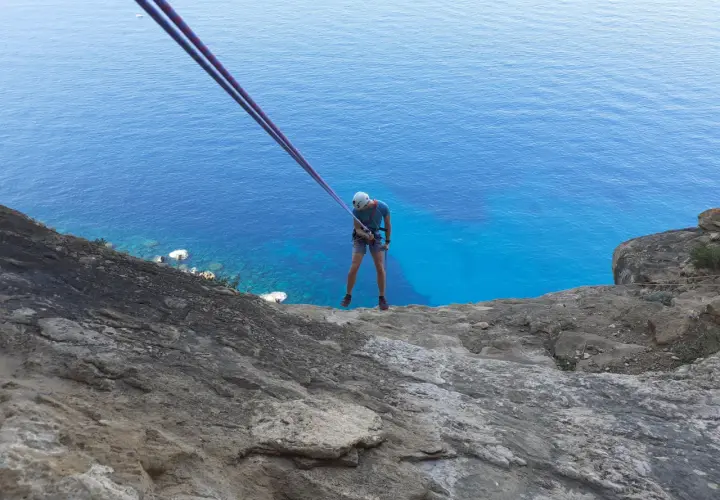 Un grimpeur se prépare pour une descente en rappel au Cap Canaille, avec la mer d'un bleu intense en contrebas. L'escalade offre une vue spectaculaire.