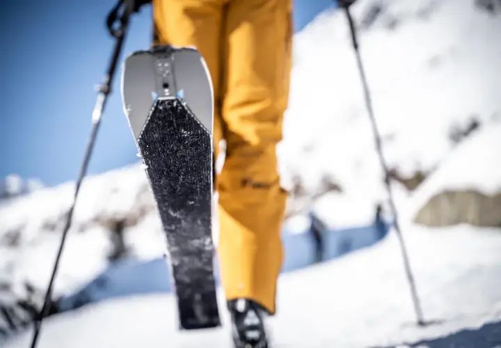 Un skieur en pantalon jaune se prépare à gravir une pente enneigée, sa peau de phoque prête à adhérer à la neige.