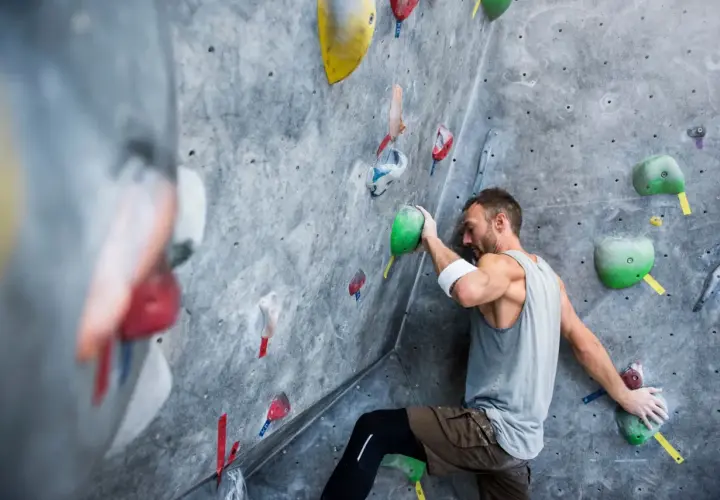 Un grimpeur concentré sur un mur d'escalade, cherchant la prise parfaite. Une scène d'escalade qui pourrait bien finir en humour si la prise glisse !