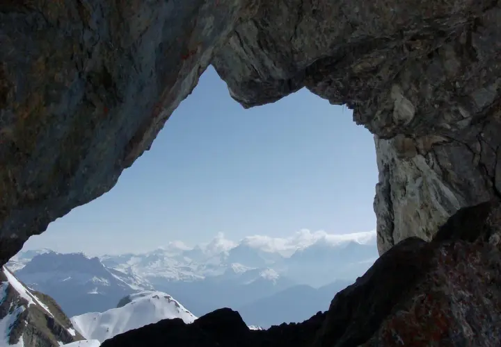 Vue spectaculaire sur les montagnes enneigées depuis le "Trou de la Mouche", un passage rocheux offrant une perspective unique lors d'une randonnée.