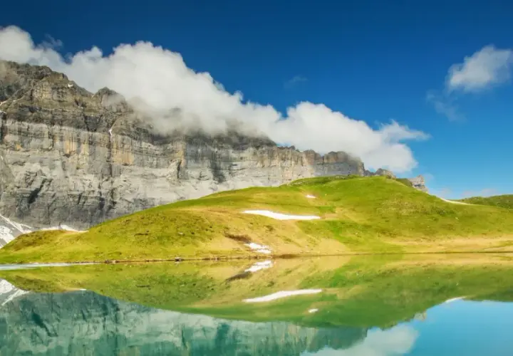 Reflets parfaits d'une montagne imposante et d'une colline verdoyante dans un lac alpin paisible, évoquant la sérénité du tour des Fiz.